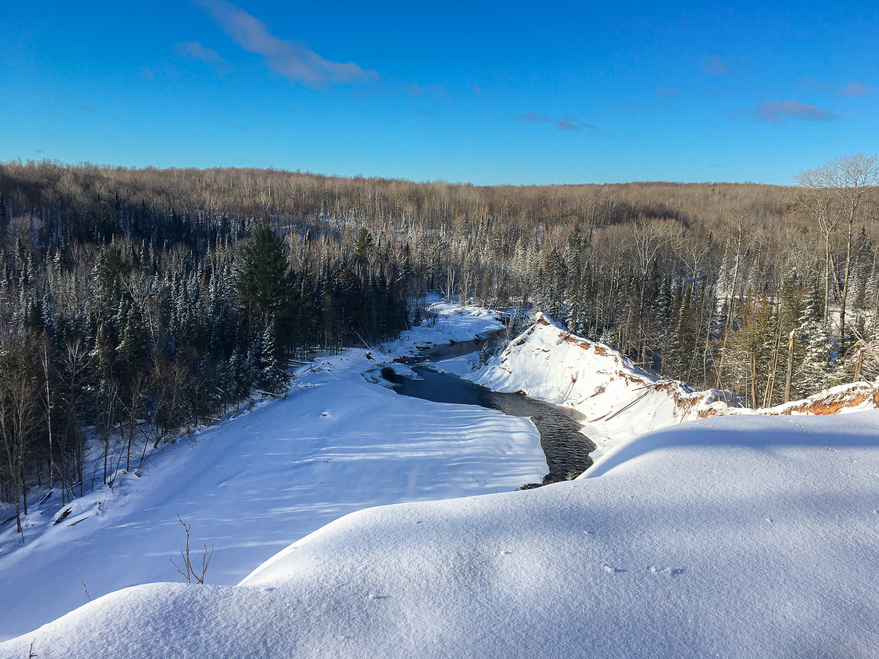 A snowy forest valley with a winding river and snow-covered banks under a blue sky.